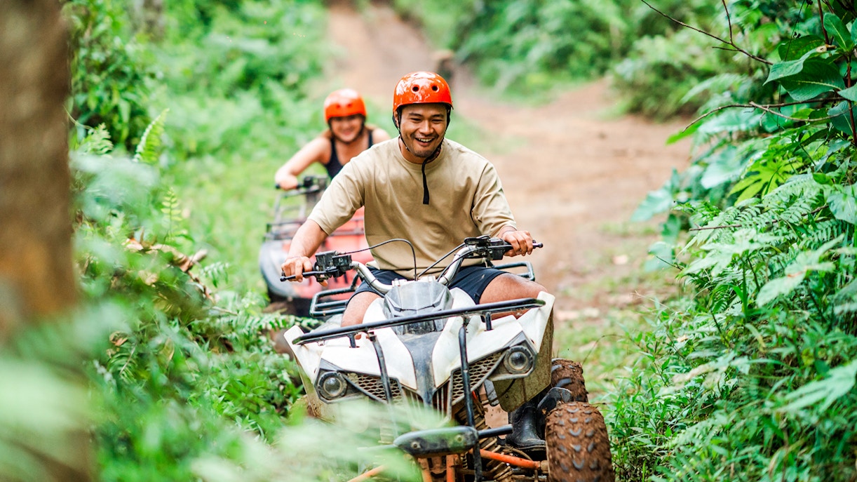 Couple riding ATVs through lush forest trail in Bali.