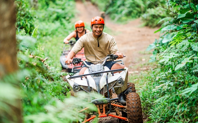 Couple riding ATVs through lush forest trail in Bali.