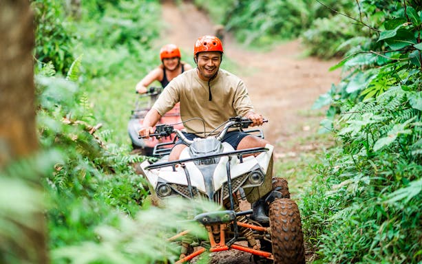 Couple riding ATVs through lush forest trail in Bali.