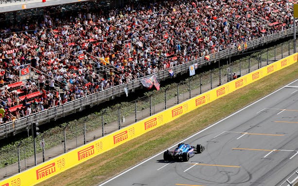 Formula 1 car racing on track with crowd at Circuit de Barcelona-Catalunya.