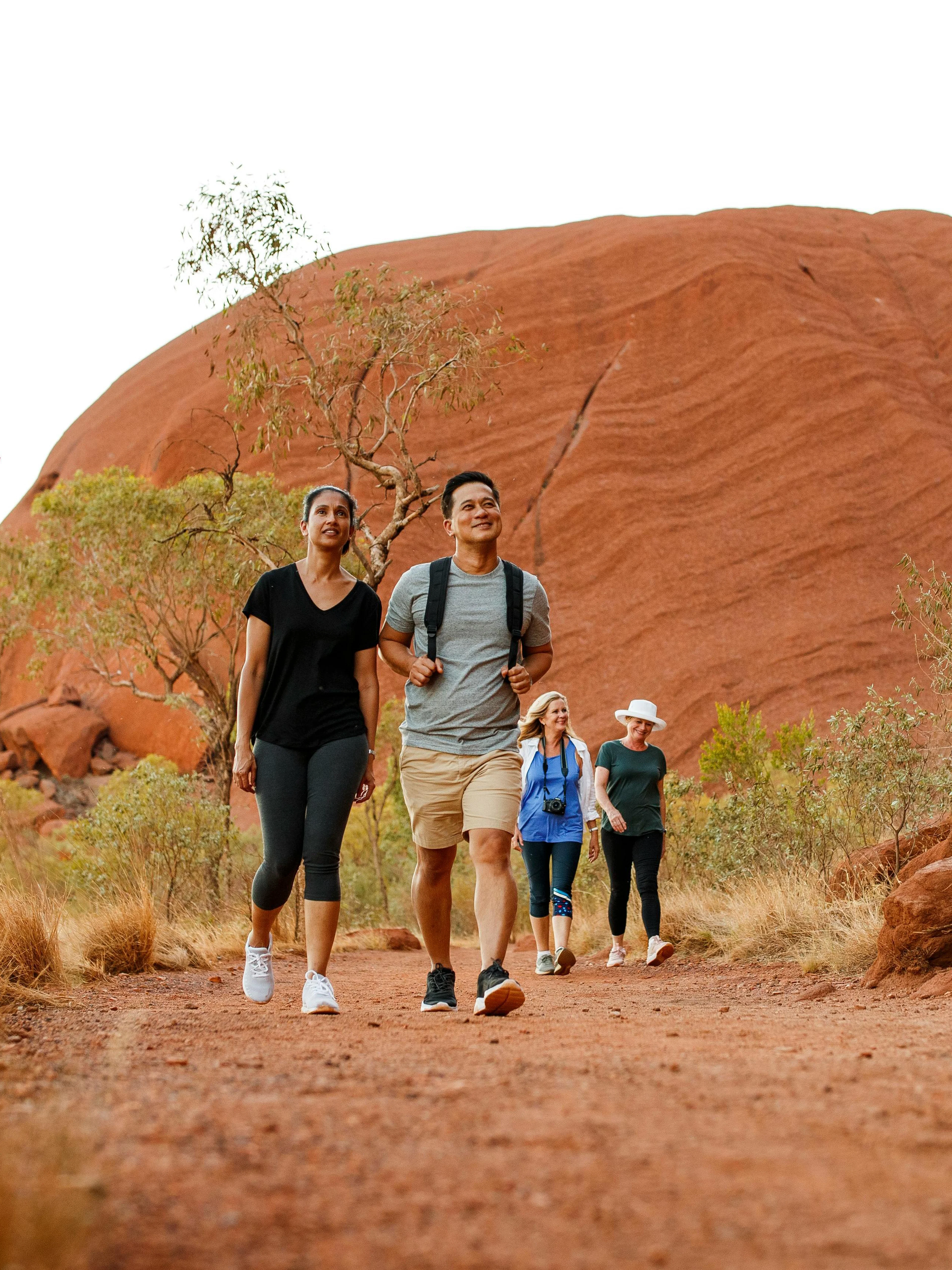 Group walking along Uluru base at sunrise during guided tour, Australia.
