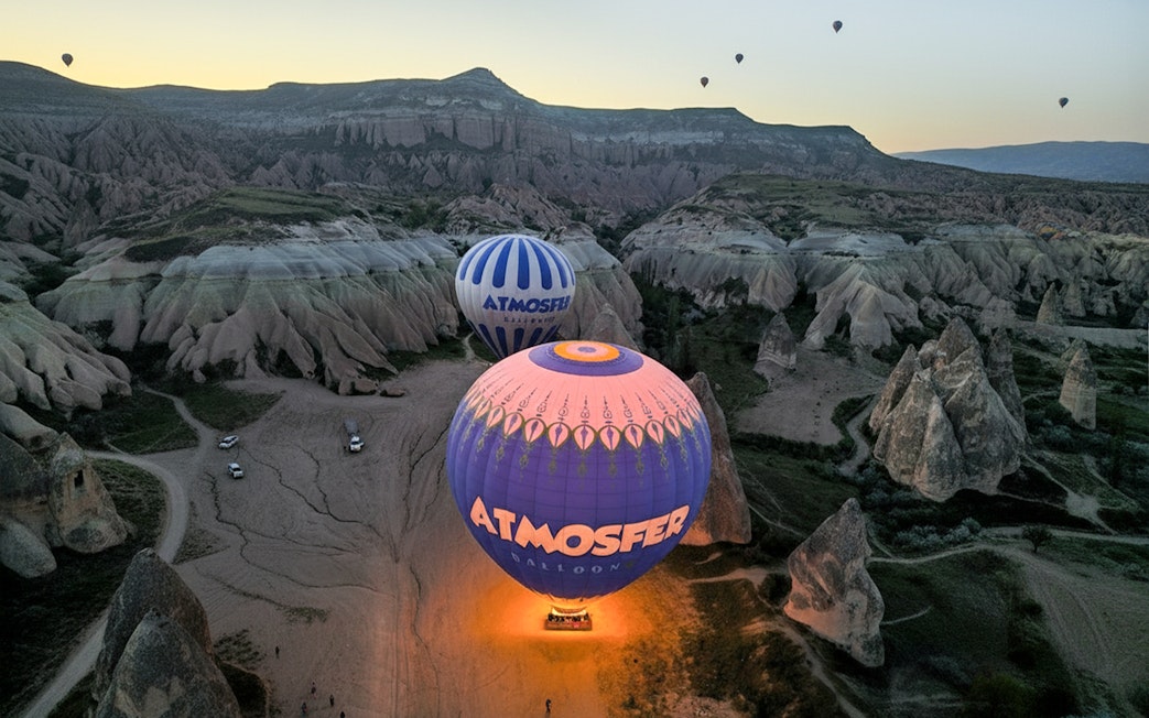 Hot air balloons from Atmosfer soaring over Cappadocia's unique rock formations at sunrise.