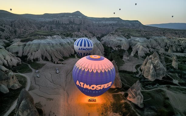 Hot air balloons from Atmosfer soaring over Cappadocia's unique rock formations at sunrise.