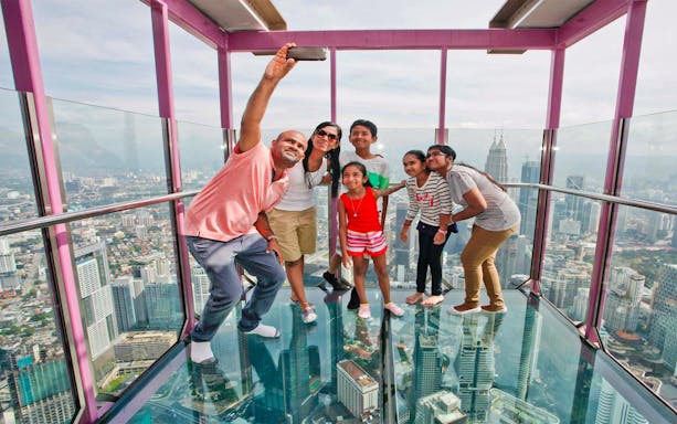 Family taking a selfie on the KL Tower SkyBox with cityscape views.
