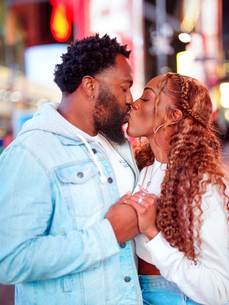 Couple kissing during a proposal on a vibrant city street at night.
