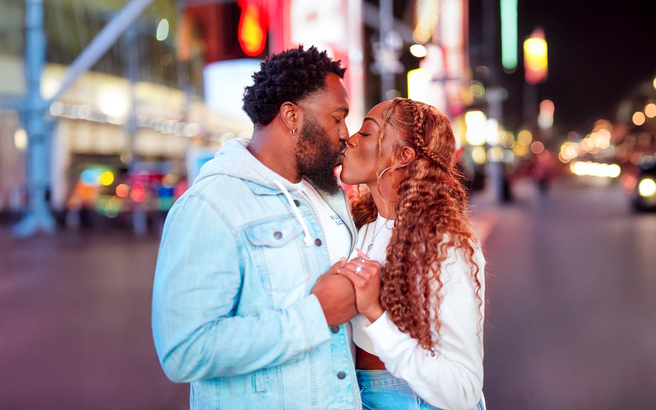 Couple kissing during a proposal on a vibrant city street at night.