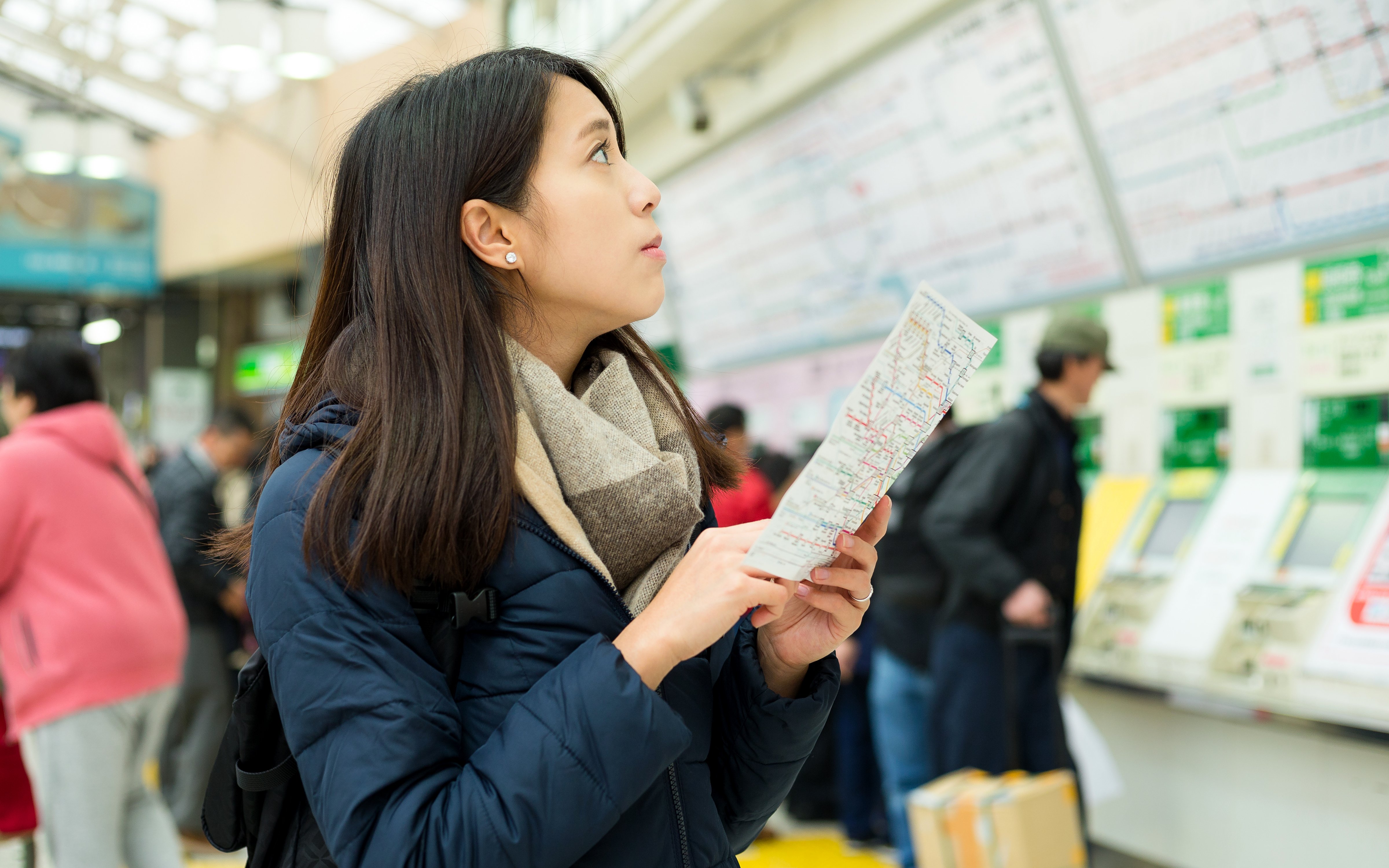 Woman holding a map in a busy train station, looking for directions.