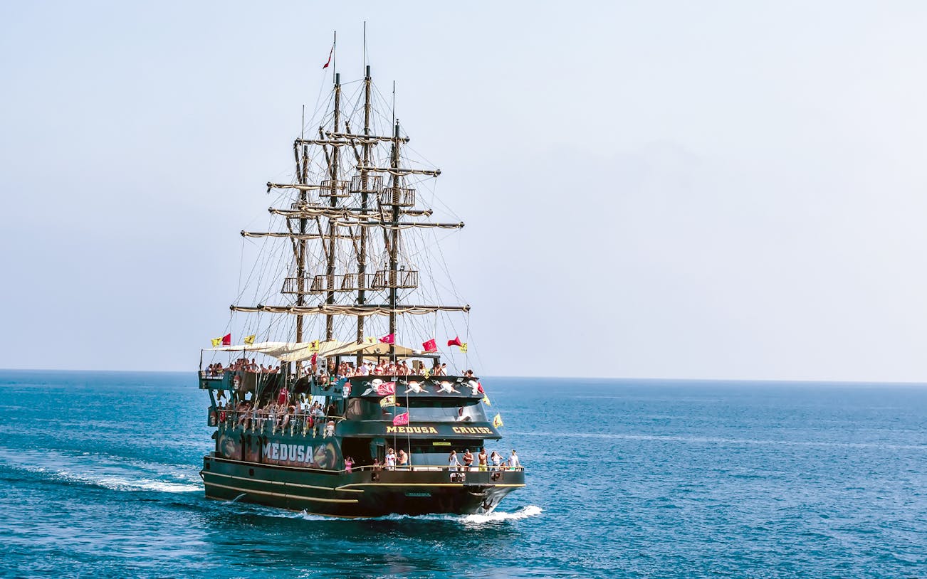 Pirate-themed boat sailing from Kemer to Phaselis Bay with passengers on deck.
