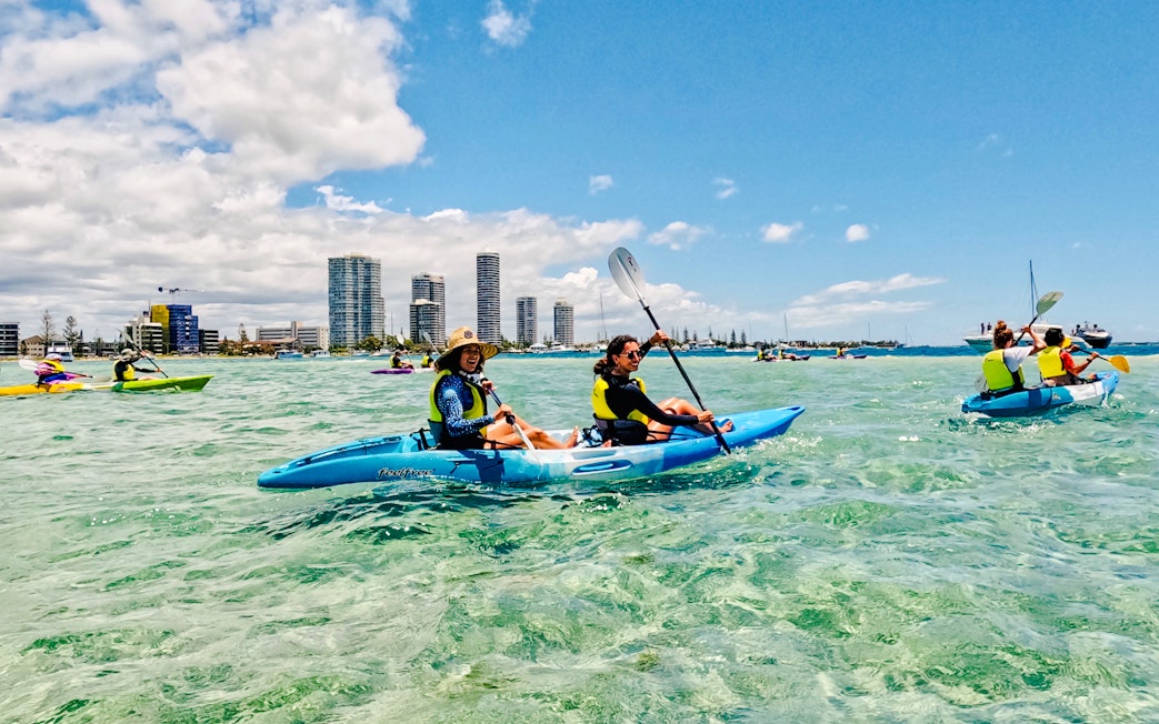 Kayakers paddling in Broadwater, Gold Coast with city skyline in the background.