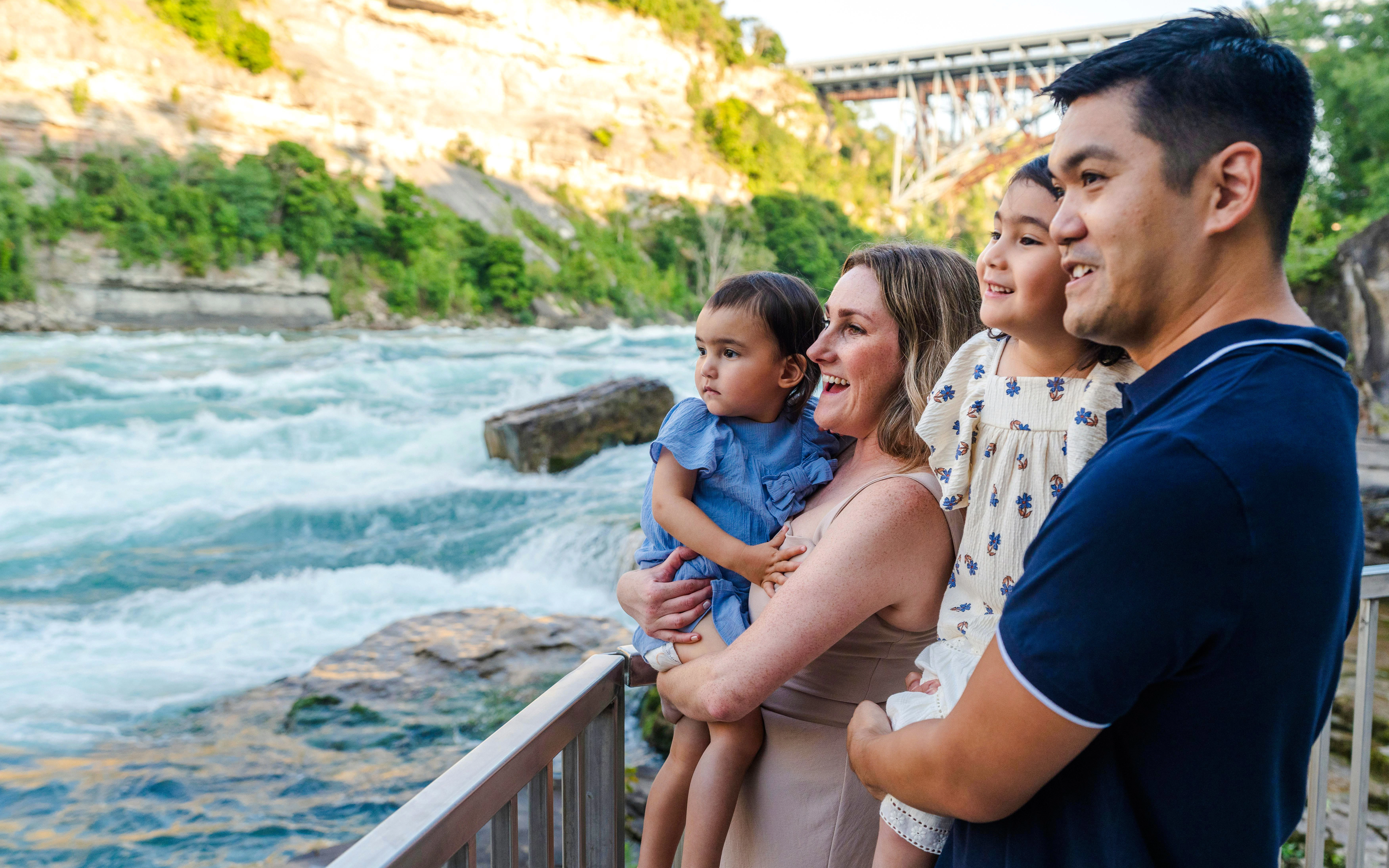 Family enjoying the view of white water rapids from a riverside railing.