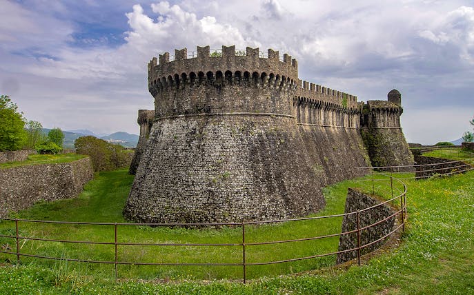 Fortezza di Sarzanello, a medieval fortress in Sarzana, Italy, with stone walls and lush surroundings.