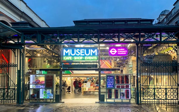 Entrance to London Transport Museum with neon signs and visitors inside.