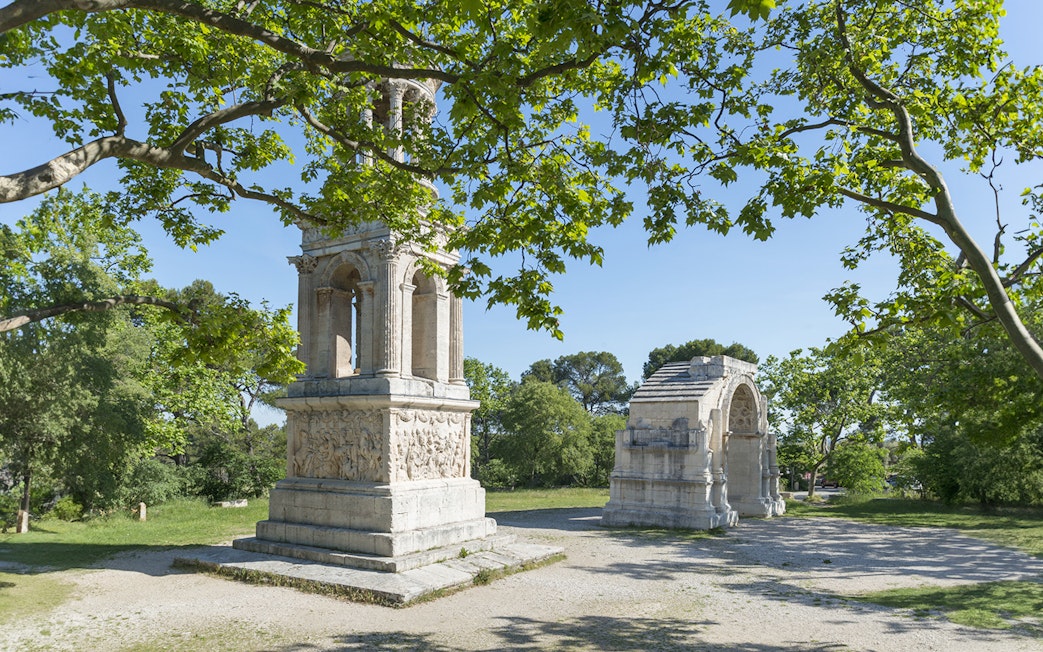 Glanum Archaeological Site entrance with Roman ruins and lush greenery.