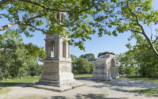 Glanum Archaeological Site entrance with Roman ruins and lush greenery.
