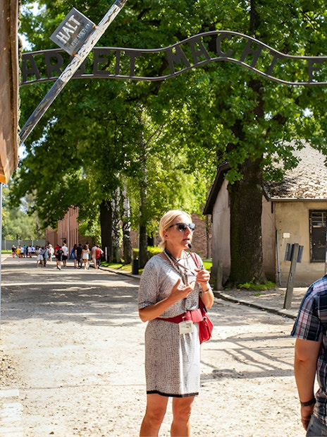 Tour guide leading visitors under the "Arbeit macht frei" gate at Auschwitz Birkenau.