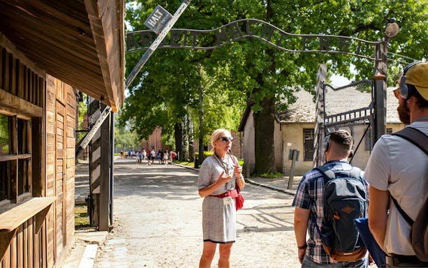 Tour guide leading visitors under the "Arbeit macht frei" gate at Auschwitz Birkenau.