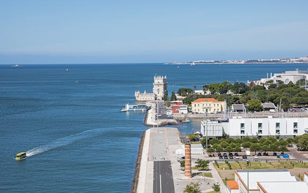 Belém Tower on Lisbon's waterfront with surrounding buildings and ocean view.