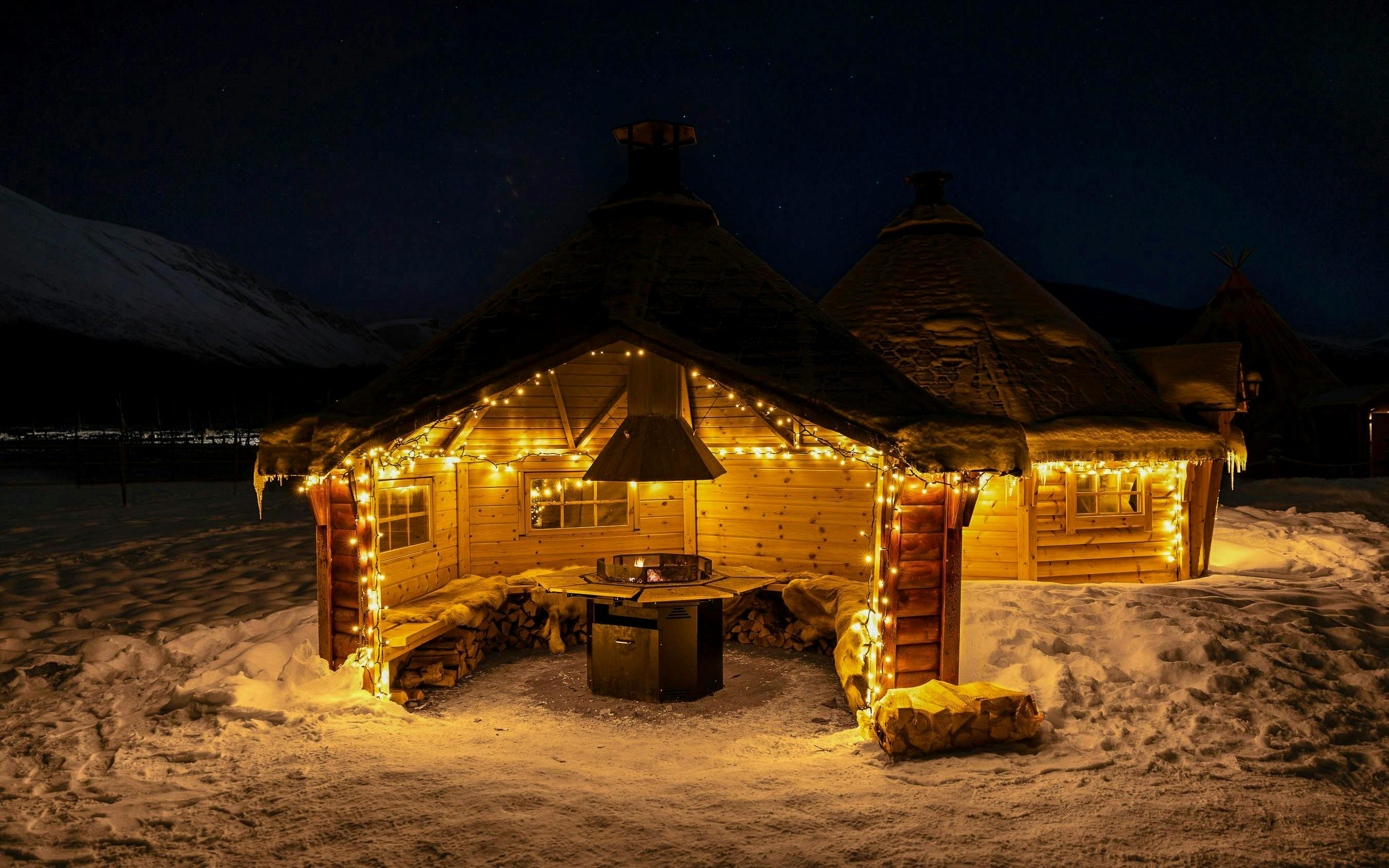 Wooden hut with lights in snowy Tromso, Norway, near reindeer feeding area.