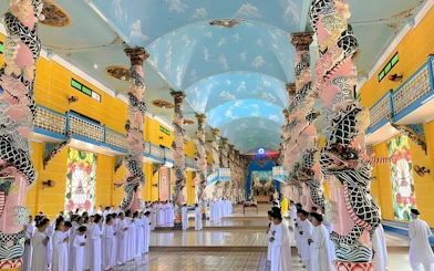 Cao Dai temple interior with worshippers in white robes, Tay Ninh, Vietnam.