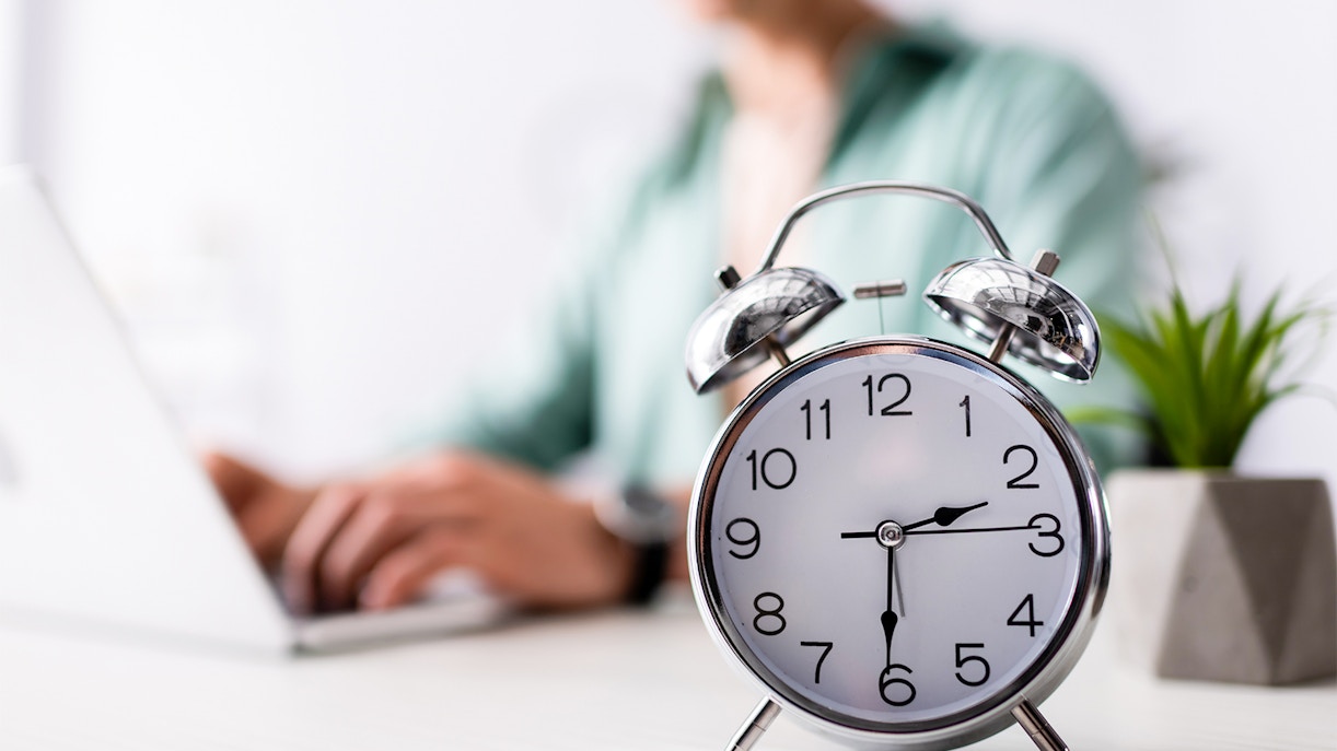 Alarm clock on desk with person using laptop, related to Skydive Melbourne timings