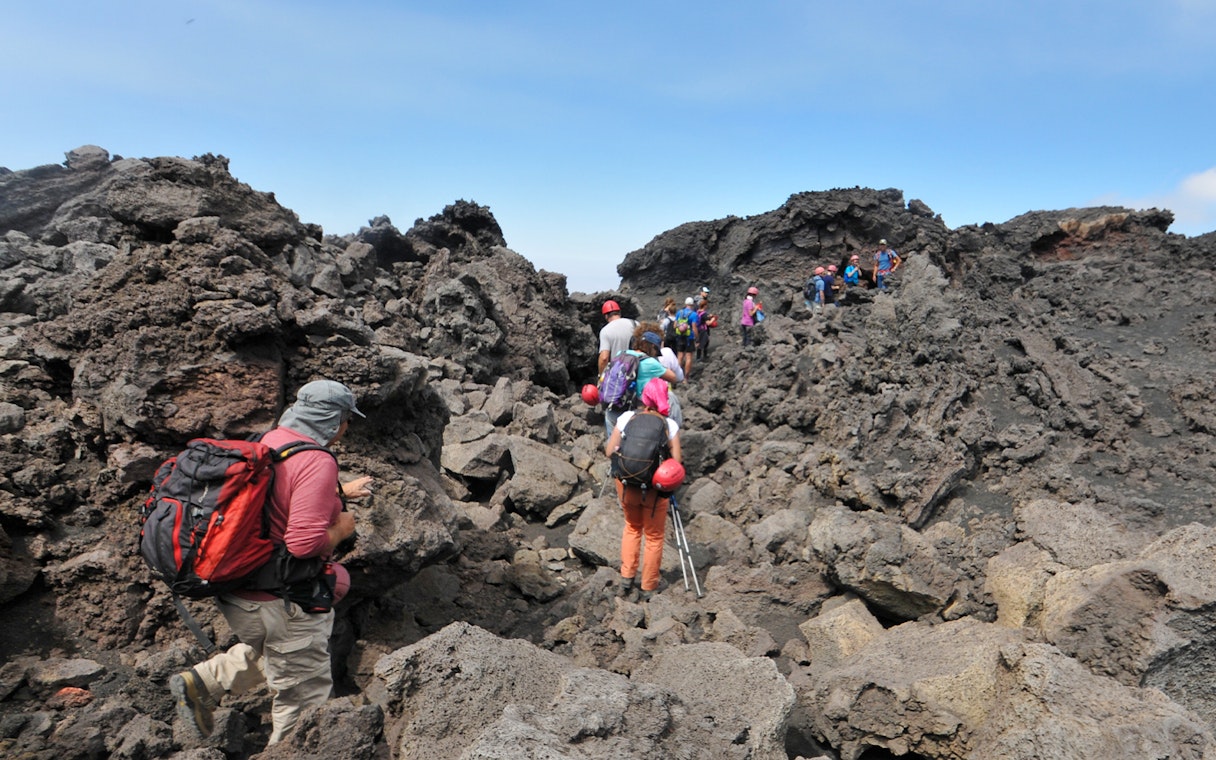 Hikers navigating rocky terrain on Mount Etna, Sicily.