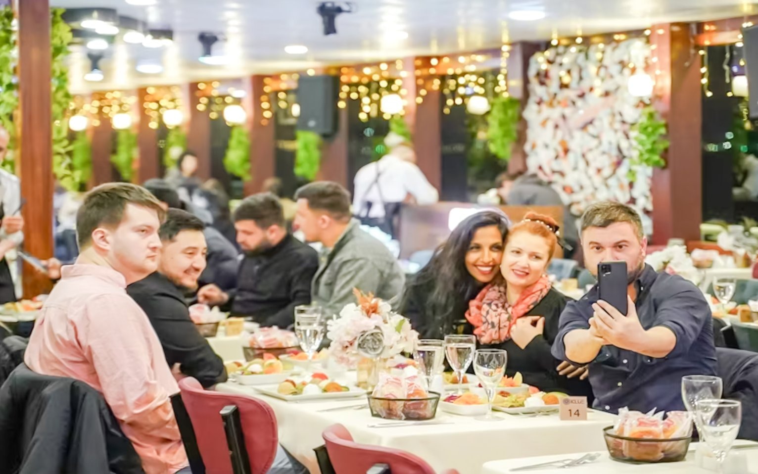 Guests enjoying a Turkish dinner on a Bosphorus night cruise, taking a selfie at a decorated table.