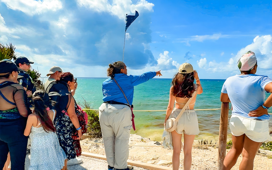 Tourist guide pointing at Tulum Beach with group of tourists.