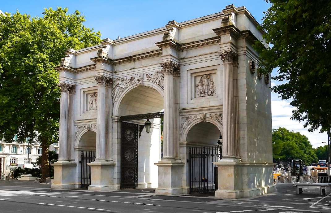Marble Arch in London with detailed carvings and surrounding trees.