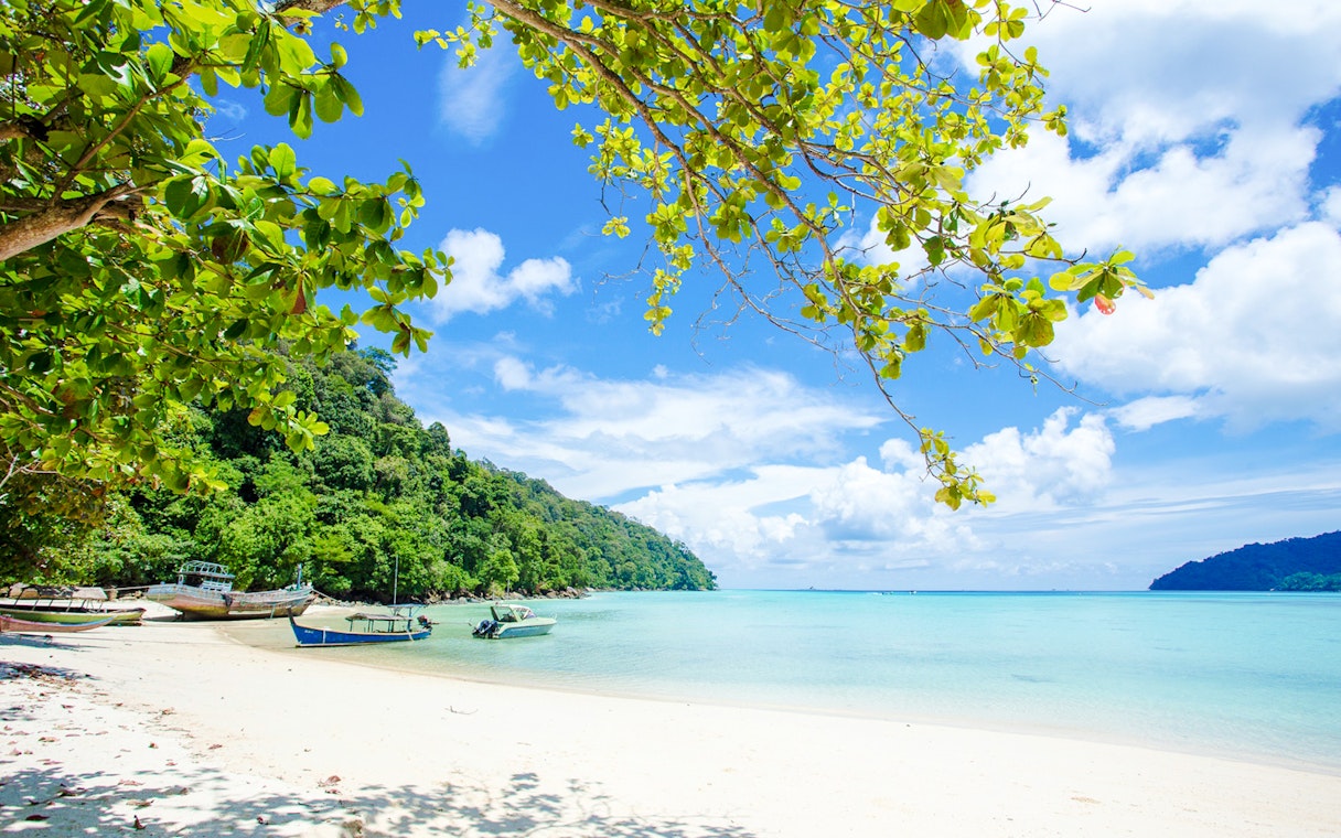 Boats on white sand beach with clear blue water in Surin Islands.