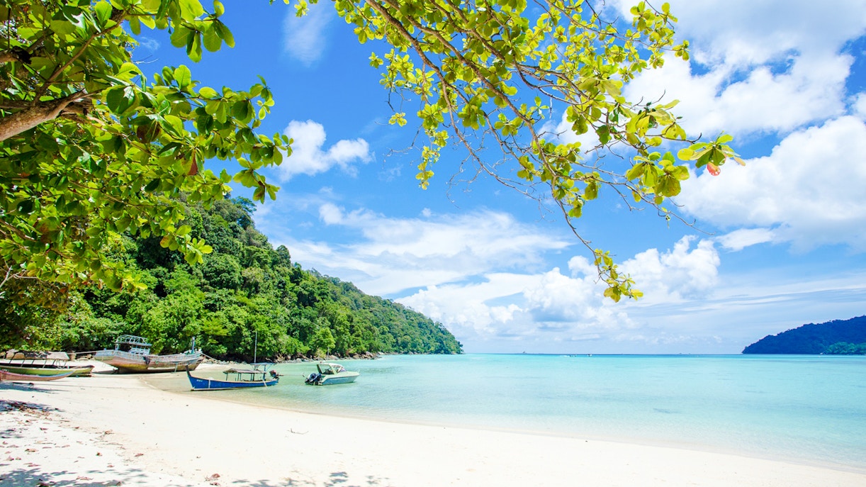 Boats on white sand beach with clear blue water in Surin Islands.