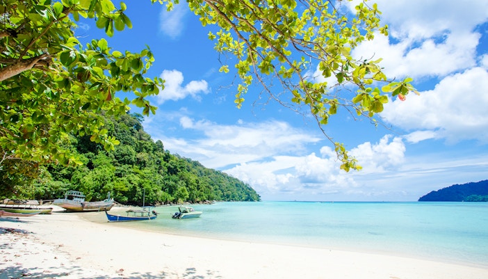 Boats on white sand beach with clear blue water in Surin Islands.