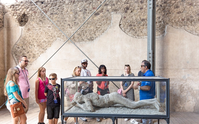 Tour guide explaining Pompeii victim cast to tourists.
