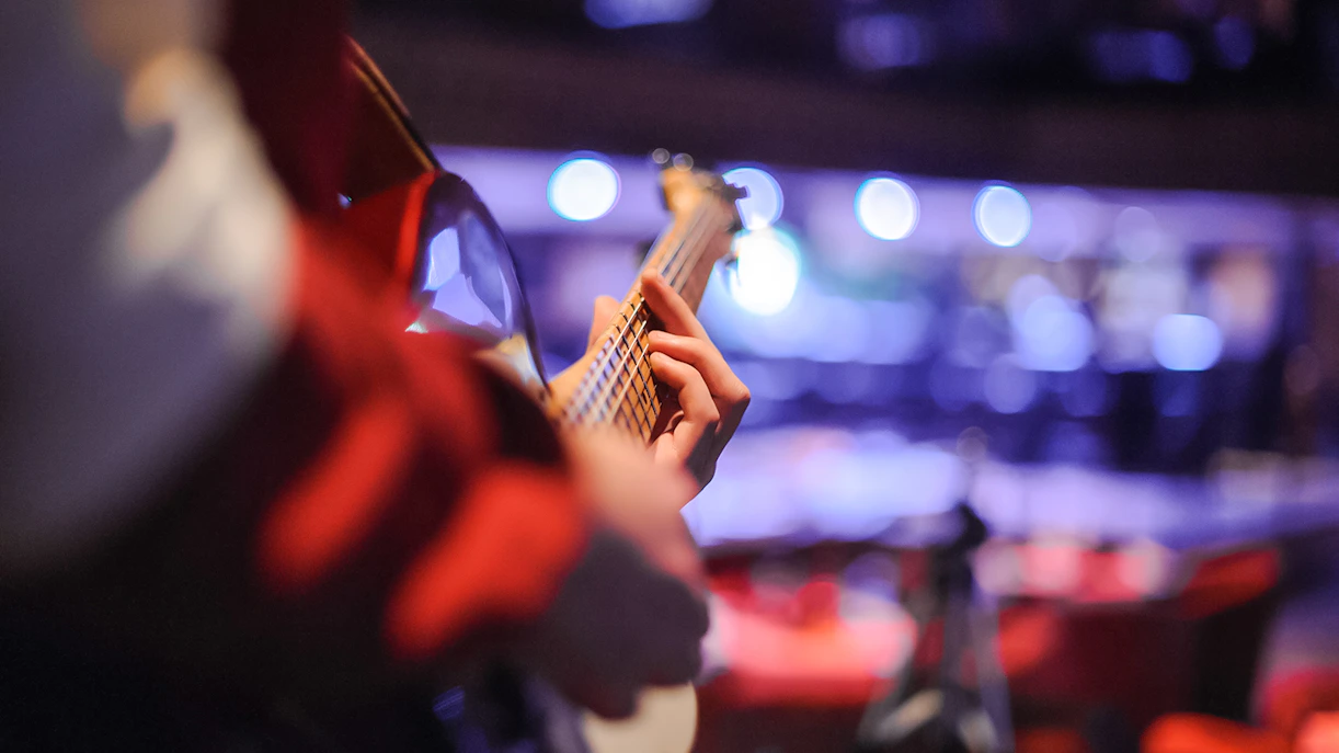 Guitarist performing live music on stage with blurred audience in background.