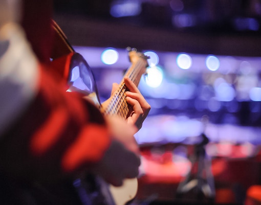 Guitarist performing live music on stage with blurred audience in background.