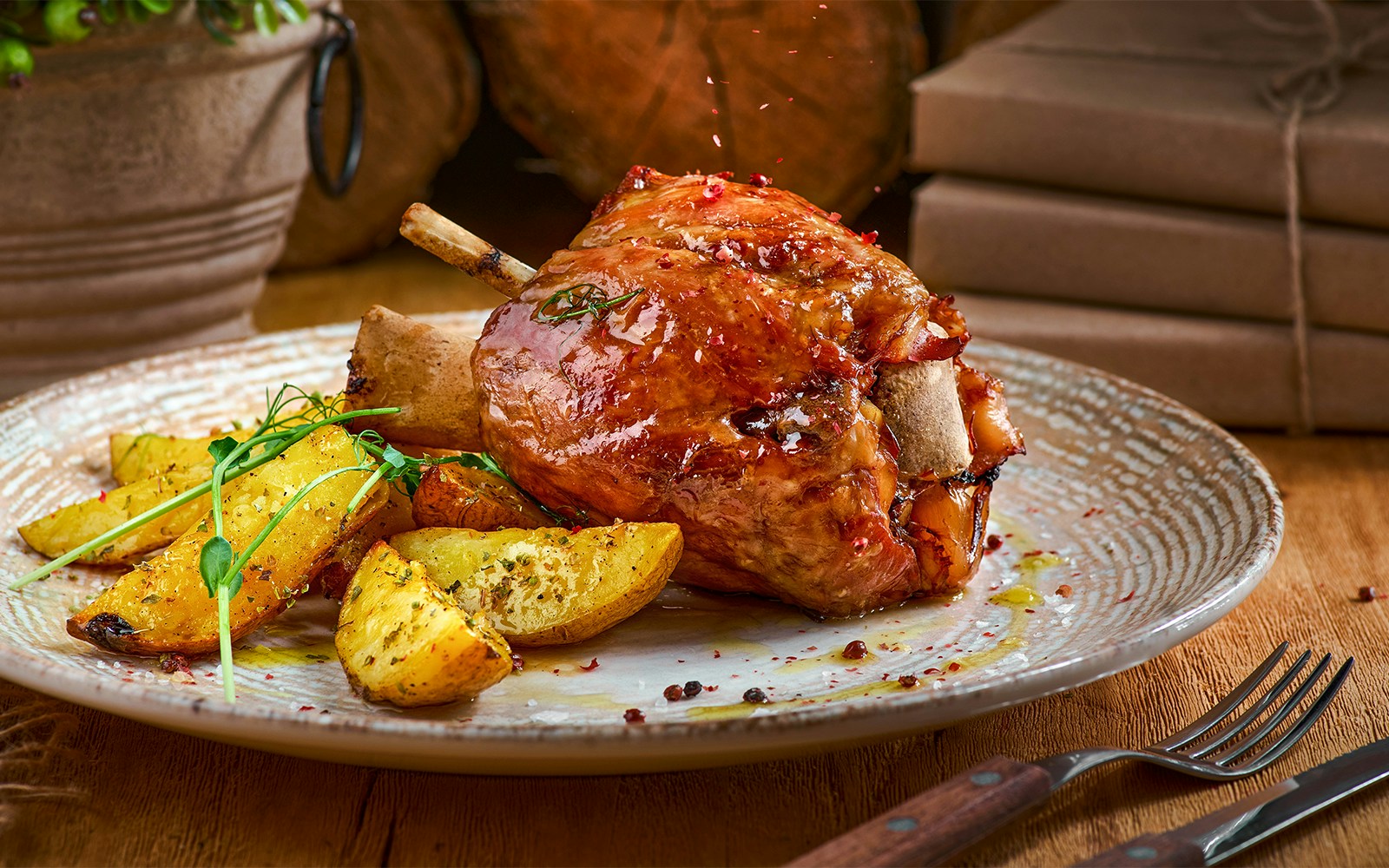 Pork knuckle with baked potatoes on a plate, close-up view.
