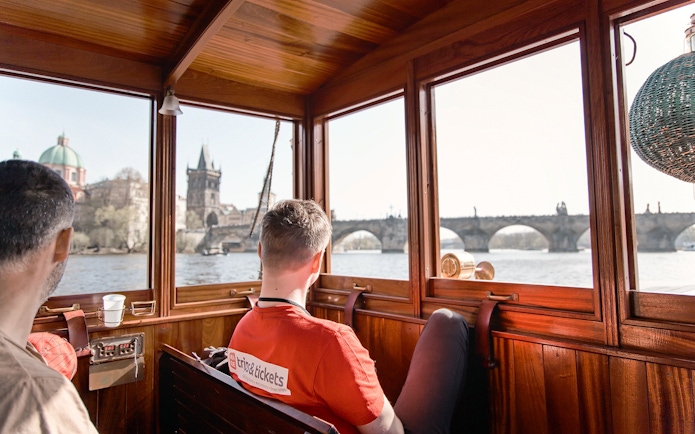 Tourists on a Vltava River cruise view Charles Bridge and Prague Castle from a boat.