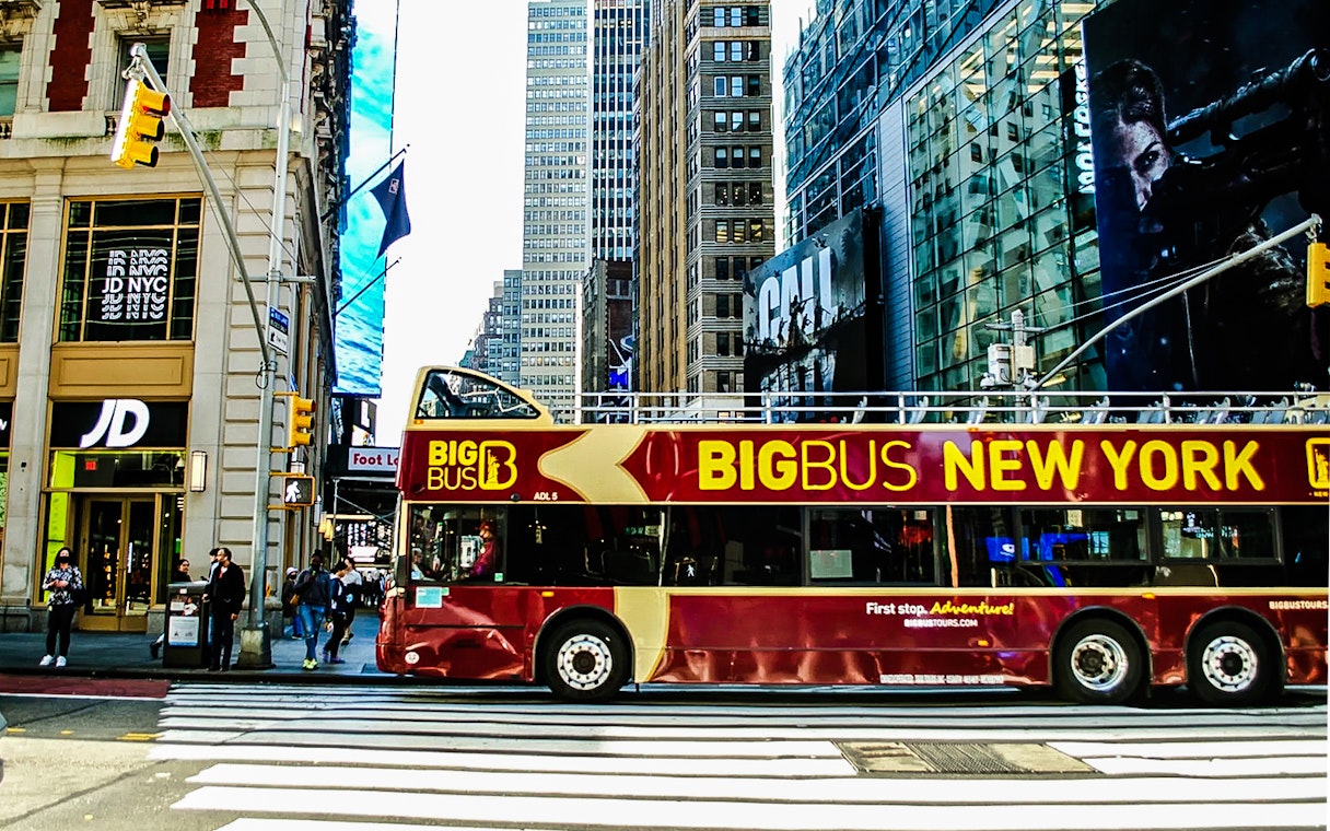 Big Bus New York tour bus on a city street with skyscrapers in the background.