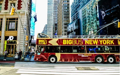 Big Bus New York tour bus on a city street with skyscrapers in the background.