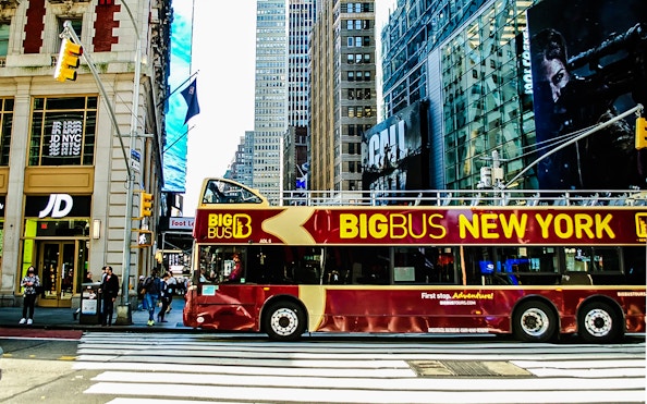 Big Bus New York tour bus on a city street with skyscrapers in the background.