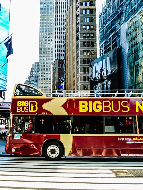 Big Bus New York tour bus on a city street with skyscrapers in the background.