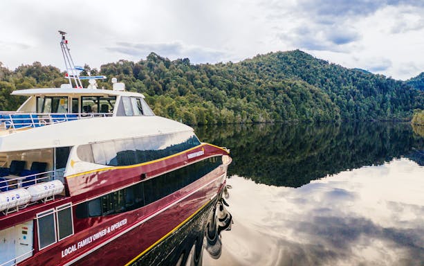 Cruise boat on Gordon River with forested hills in Strahan, Tasmania.