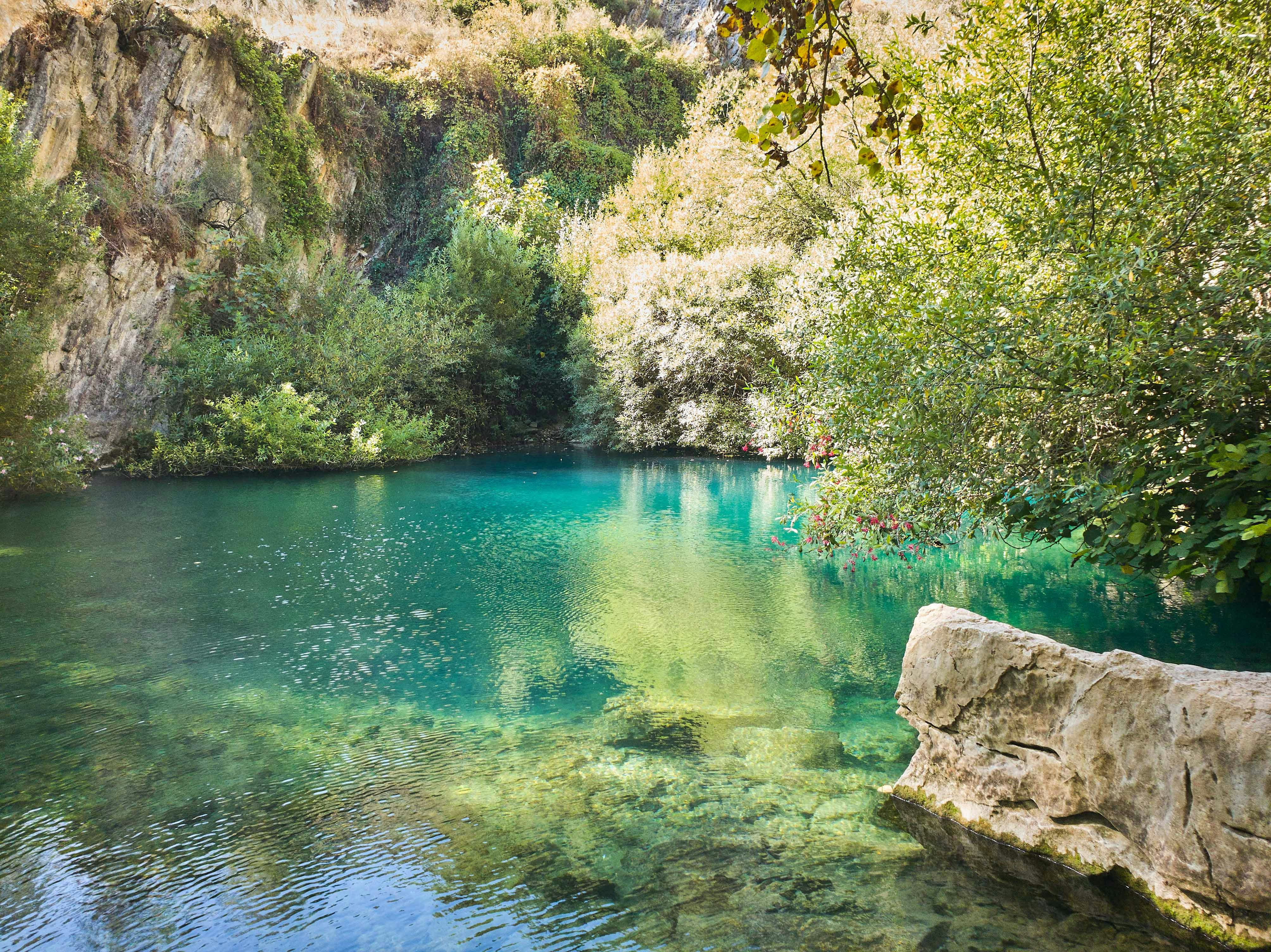 Green Cave in Croatia with clear turquoise water surrounded by lush greenery and rocky cliffs.