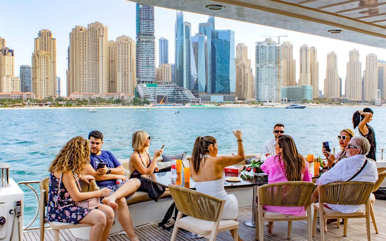 Tourists enjoying a Superyacht TriDeck cruise with Dubai skyline in the background.