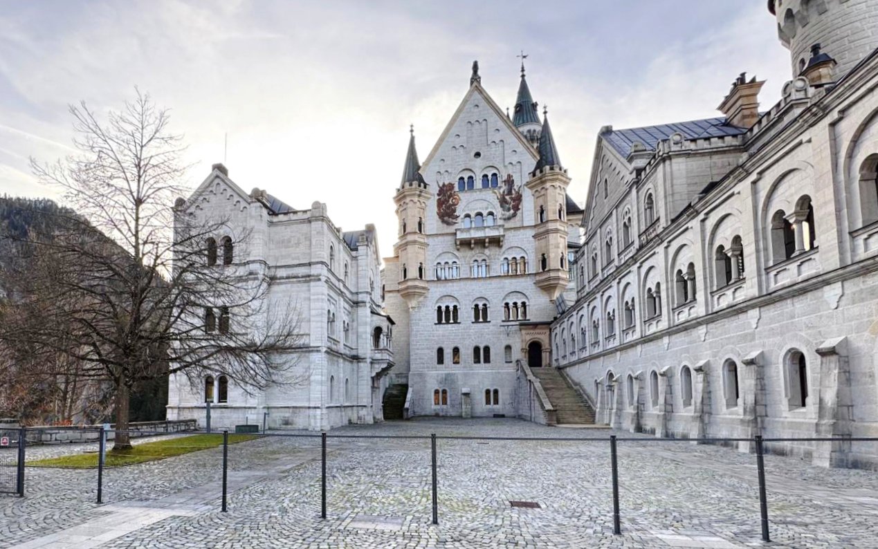 Courtyard view of Neuschwanstein Castle with stone facade and arched windows.