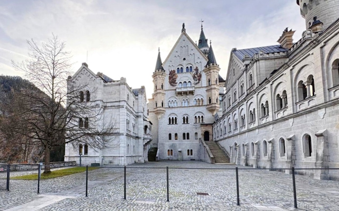 Courtyard view of Neuschwanstein Castle with stone facade and arched windows.