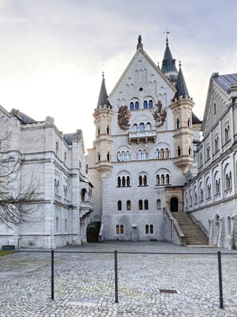 Courtyard view of Neuschwanstein Castle with stone facade and arched windows.