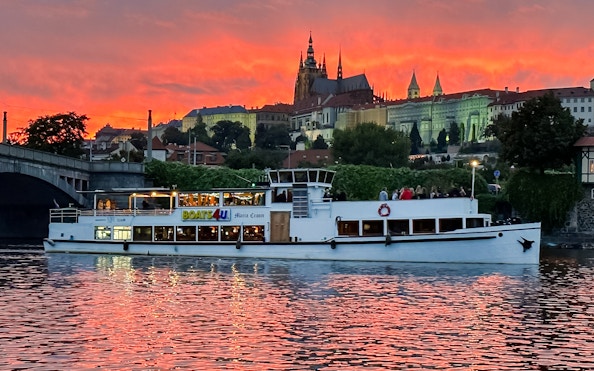 Historic ship Maria Croon on Vltava River with Prague Castle at sunset.