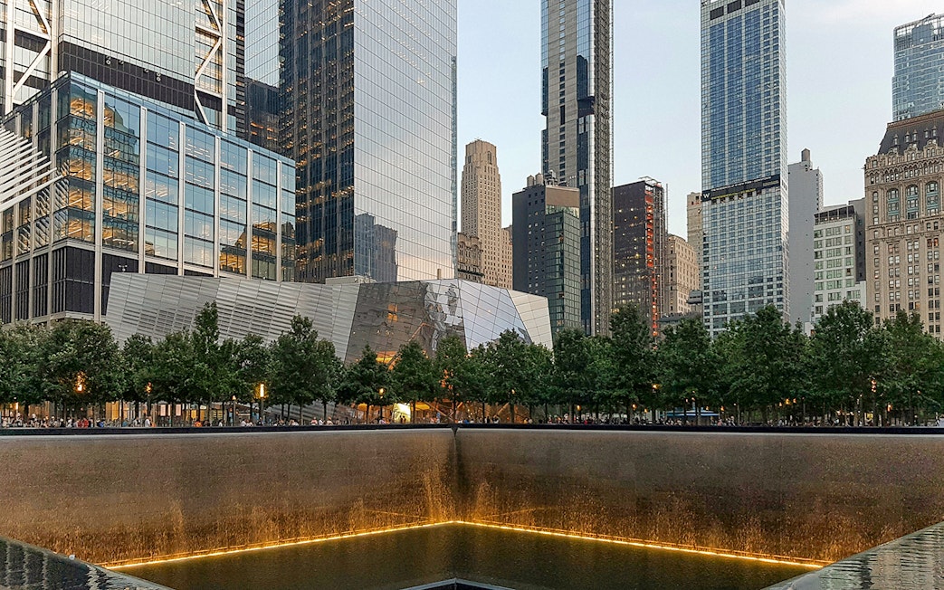 9/11 Memorial reflecting pool with museum entrance and skyscrapers in New York City.