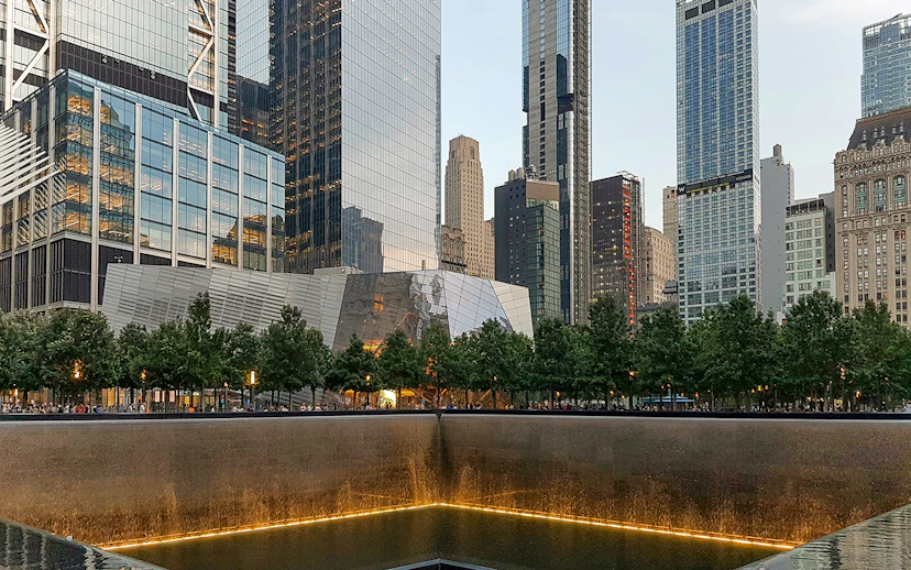 #9/11 Memorial reflecting pool with museum entrance and skyscrapers in New York City.
