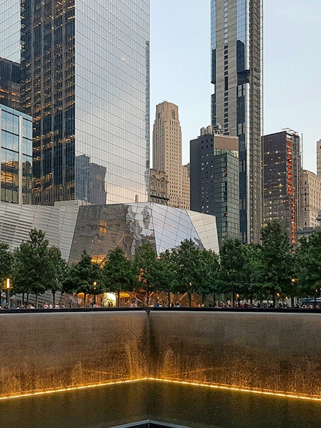 9/11 Memorial reflecting pool with museum entrance and skyscrapers in New York City.